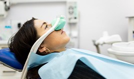 Profile view of reclined woman with dark hair with green nitrous oxide mask over nose
