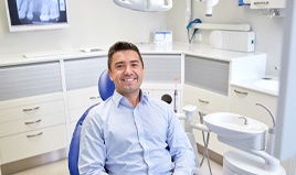 Man smiling in dental chair wearing blue shirt