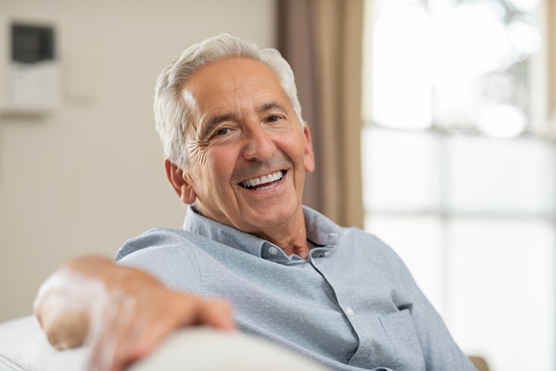 Man with implant dentures leaning on his couch