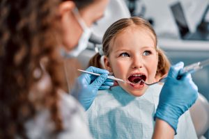 Girl in pigtails with blue eyes sitting having dental exam by dentist wearing blue gloves
