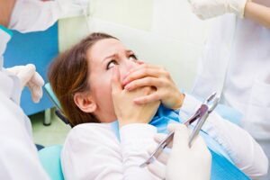 Scared woman in the dentist’s chair covering her mouth.